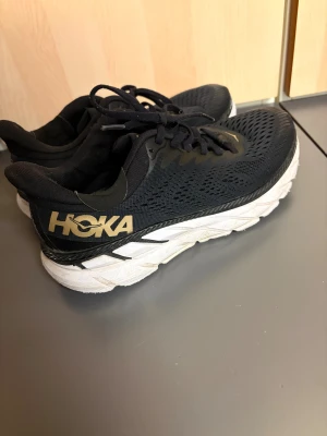 Svarta Hoka sneakers med vit sula - Säljer ett par svarta Hoka sneakers med vit och svart tjock sula. Skorna har använts ett bra tag och är storlek 40 