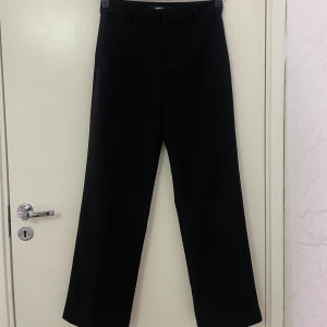Svarta kostymbyxor Gina Tricot 34 - Klassiska svarta kostymbyxor från Gina Tricot i storlek 34. Byxorna har raka ben, bälteshällor och diskreta fickor fram och bak. De är mid waist, Snyggt midjeformat och stilren look som passar till många olika outfits. Passar även någon som har 36 i storlek. 