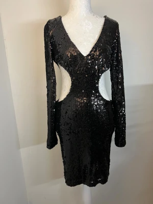 Klänning - Svart kort paljettklänning från Fashion Nova med lång ärm, v-ringning och cut-out midja. Storlek S. Klänningen har dragkedja i ryggen och en figurnära passform. Använd en gång och i utmärkt skick 🖤