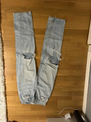 Ljusblå ripped jeans från g perfect jeans - Säljer ett par högmidjade ljusblå jeans från g perfect jeans i storlek 32. Modellen har raka ben, slitna detaljer och stora hål vid knäna för en edgy look. Klassisk femficksdesign och fransiga benslut. Perfekt för dig som gillar streetstyle. Säljer då den ej används längre