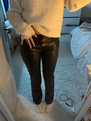 Skinnbyxor - Snygga svarta byxor i skinnimitation med rak passform och klassisk midja. De har fickor fram och stängs med dragkedja och knapp. Perfekta för dig som vill ha en cool och trendig look.