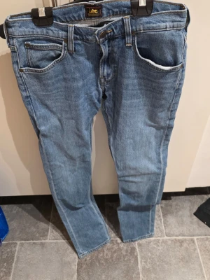 Lee Luke ljusblå jeans W29 L32 - Säljer ett par Lee Luke jeans i ljusblå tvätt med klassisk femficksdesign och bruna detaljer på bakfickan. Jeansen har rak passform och är tillverkade i bomull. Perfekt för dig som gillar en enkel och stilren look.