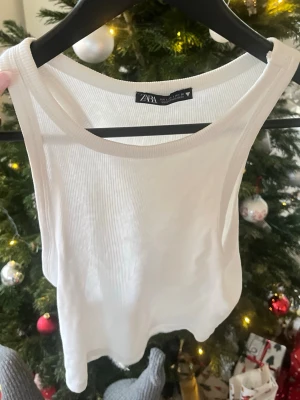 Vit ribbad linnetopp från Zara - Säljer en fräsch vit ribbad linnetopp från Zara i storlek M. Toppen är ärmlös med rund halsringning och har en croppad passform. 