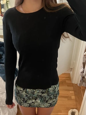 Svart långärmad tröja  - En stilren svart långärmad tröja med rund hals. Tröjan har en slim passform och är gjord i mjuk bomull som sitter skönt mot kroppen. Perfekt att matcha med kjol eller jeans för en enkel och snygg look.