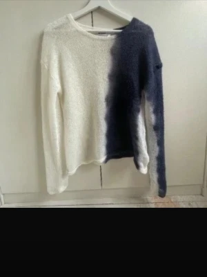 Weekday tröja  - Säljer en unik stickad tröja med cool tvåfärgad design i vitt och mörkblått. Tröjan har långärmad passform och är mjuk och fluffig i materialet. Perfekt för dig som gillar att sticka ut med din stil och vill ha något annorlunda i garderoben.
