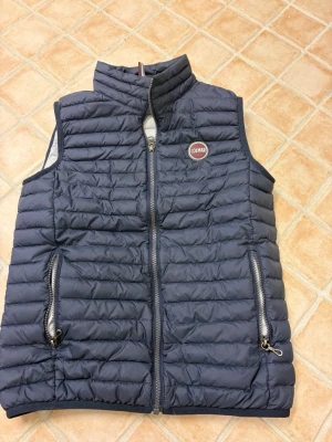 Mörkblå dunväst från Colmar - Säljer en mörkblå quiltad dunväst från Colmar i storlek 14Y/166. Västen har två fickor med dragkedja, hög krage och ett snyggt Colmar-märke på bröstet. Perfekt att slänga över en hoodie när det är kyligt ute.