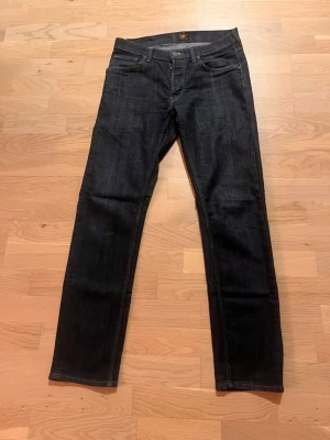 Mörkblå Lee jeans med raka ben - Snygga mörkblå jeans från Lee med klassisk femficksdesign och raka ben. Jeansen har kontrastsömmar i gult och knäppning med knappar framtill. Materialet är slitstarkt jeans och passformen är normal. Perfekt för dig som gillar tidlös stil och vill ha ett par jeans som funkar till allt. W31/L32