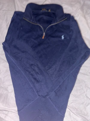 Marinblå half zip tröja Polo Ralph Lauren - Snygg marinblå tröja från Polo Ralph Lauren i storlek M. Tröjan har en klassisk half zip-dragkedja och den ikoniska broderade loggan på bröstet. Tillverkad i mjuk bomull med ribbade muddar och krage. Perfekt för chill dagar och enkel att matcha med jeans.