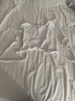 Vit omlottopp med snörning - Säljer en vit omlottopp med snörning i midjan och korta ärmar. Toppen har en croppad passform och är tillverkad i mjukt bomullsmaterial. Perfekt att styla med jeans eller kjol för en fräsch look.