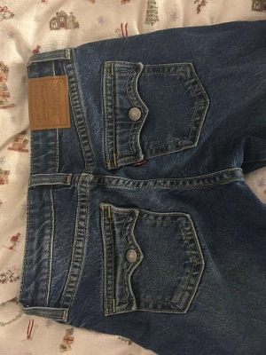Levi's Noughties Bootcut jeans blå - Säljer ett par Levi's Noughties Bootcut jeans i klassisk blå denim. Jeansen har snygga fickor med lock och knapp bak, kontrastsömmar och bootcut-ben. Perfekta för dig som gillar retrovibbar och vill ha en cool siluett.