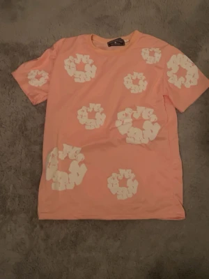 Ljusrosa t-shirt med vit blommönster - Säljer en ljusrosa t-shirt från Second/Layer med coola vita blommönster över hela tröjan. T-shirten har korta ärmar och är gjord i mjuk bomull, perfekt för dig som gillar färg och unika prints.