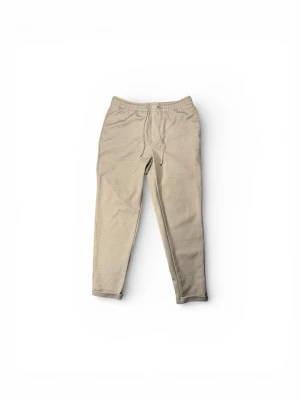 Beige kostymbyxor från Zara - Snygga beige kostymbyxor från Zara med elastisk midja och snörning framtill. Byxorna har raka ben, fickor både fram och bak samt är tillverkade i mjukt bomullsmaterial. Perfekta för chill dagar och enkel att matcha med hoodies eller t-shirts.