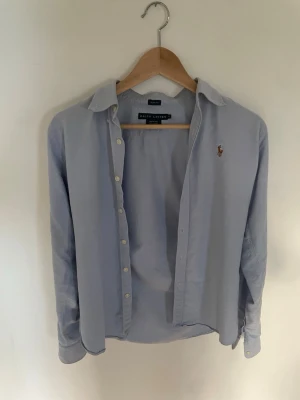 Blå skjorta från Ralph Lauren - Snygg ljusblå skjorta i ett väldigt bra skick från Ralph Lauren. Kragen på skjortan har ett rosa randigt mönster vilket enligt mig höjer skjortan till en högre nivå! Detta är en barn skjorta, storleken på skjortan är alltså inte storlek M för vuxna utan storlek M för barn. Som man kan se på sista bilden så har en galge färgat av sig. Det har visserligen inte gått bort helt i tvättmaskinen men man ska nog kunna få bort det med lite nogare tvättning eller liknande.