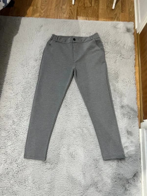 Grå mjukisbyxor med slim fit - Säljer ett par grå mjukisbyxor med slim passform. Byxorna har resår i midjan, bälteshällor, knapp framtill och fickor både fram och bak. Perfekta för chill dagar eller när du vill vara bekväm men ändå se stilren ut.