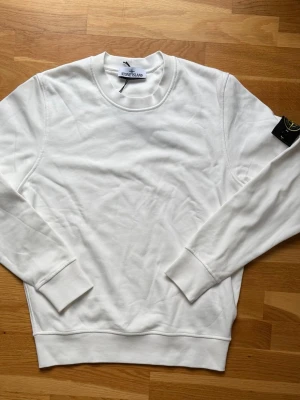 Stone Island sweatshirt (Vit) S - "Vit Stone Island-sweatshirt i storlek S. Klassisk modell med rund hals och logomärke på ärmen. Mjukt material av hög kvalitet, perfekt för vardagsbruk. I mycket bra skick utan fläckar eller skador."