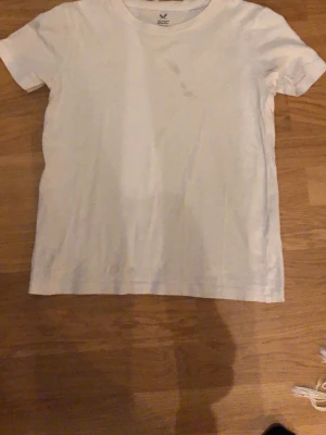 Vit basic t-shirt från SOC - En enkel vit t-shirt från SOC i storlek 134-140. Klassisk rund halsringning och korta ärmar. Tillverkad i mjuk bomull som känns skön mot huden. Perfekt till jeans eller shorts för en clean och avslappnad look.