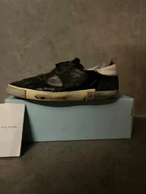 Philippe Model svarta sneakers - Svarta och vita sneakers från Philippe Model med grå detaljer och snörning. Skorna har en rund tå, platt sula och är tillverkade i skinn och mocka. Snygg logga på sidan och text på skosnörena. Perfekta för dig som gillar streetstyle och vill ha något unikt.