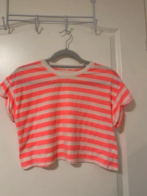 Randig croppad topp i rosa och vit - Croppad topp med breda rosa och vita ränder. T-shirten har korta ärmar och rund halsringning med vit kant