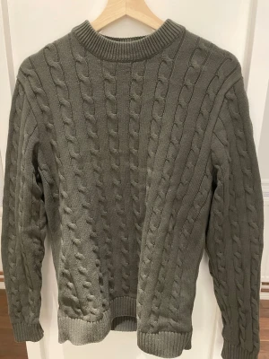 Grön kabelstickad tröja Selected Homme - Säljer en grön kabelstickad tröja från Selected Homme i storlek S. Tröjan har rund hals, ribbade muddar och långärmad passform. Materialet är mjukt och stickat, perfekt för kyliga dagar. Snygg struktur med klassiskt kabelmönster.