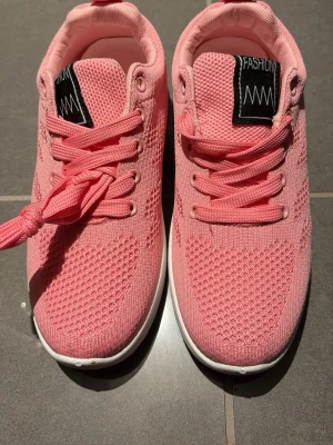 Rosa sneakers med mesh och snörning - Säljer ett par snygga rosa sneakers med stickad mesh-överdel och klassisk snörning. Skorna har en rund tå och vit platt sula som ger en sportig vibe. Perfekta för dig som gillar färg och vill ha bekväma skor till vardagen.