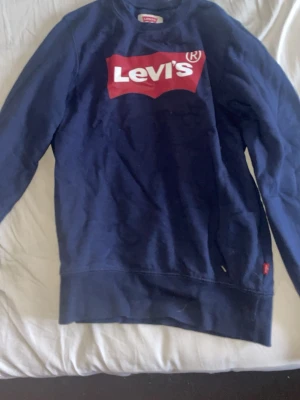 Mörkblå sweatshirt från Levi's - Säljer en mörkblå sweatshirt från Levi's med den klassiska röda loggan framtill. Tröjan har långa ärmar och rund halsringning. Perfekt för dig som gillar enkel och stilren streetwear.