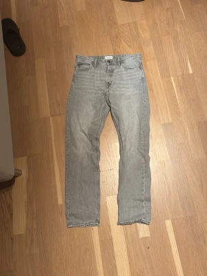 Grå loose fit jeans från Jack & Jones - Säljer ett par grå jeans från Jack & Jones, modellen Loose/Chris. De har en loose passform med raka ben och klassisk femficksdesign. Jeansen är tillverkade i bomull och har en snygg, ljusgrå tvätt som ger en chill vibe. Perfekt för dig som gillar avslappnad stil.