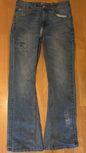 Levi's 501 blå jeans med rutig ficka - Säljer ett par Levi's 501 jeans i klassisk blå tvätt med slitna detaljer och patchad rutig bakficka i blå, beige och röd. Dessa jeans är omsydda till bootcut och har 25 cm bredd nere vid slutet av jeansen, hör av er vid frågor!