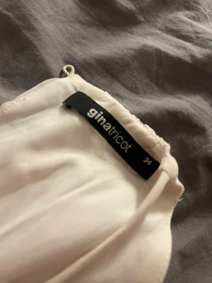 Vit långklänning från Gina Tricot - Säljer en elegant vit långklänning från Gina Tricot i storlek 34. Klänningen har ett luftigt tyg, resår i midjan och ett axelbandslöst snitt på ena sidan. Perfekt för sommarens alla tillfällen!