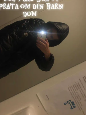 Svart Moncler maya pufferjacka med huva - Säljer en svart pufferjacka från Moncler med glansig finish och huva. Jackan har Moncler-logga på bröstet och coolt serietidningsmönster på insidan. Perfekt för dig som vill ha en varm och snygg jacka med streetkänsla. Nfc tagen funkar 