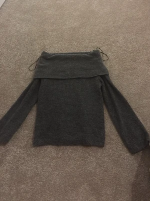 Mörkgrå offshoulder stickad tröja H&M - Säljer en mörkgrå stickad tröja från H&M i storlek XS. Tröjan har offshoulder-design med bred krage och långa ärmar. Materialet är mjukt och mysigt, perfekt för kyliga dagar. Snygg att styla med jeans eller kjol. Snörning upptill för extra detalj.