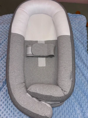 Grå och vit randig Babynest  - Säljer en mysig babyväst från Doomoo i grått och vitt med tunna ränder. Västen har en mjuk och ombonad form med ett praktiskt bälte i mitten. Perfekt för att ge extra komfort och stöd till de minsta.