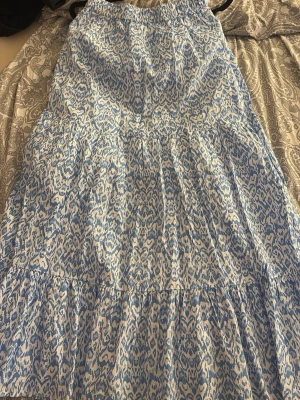Blåvit långkjol med leopardmönster - Säljer en blåvit långkjol med leopardmönster. Kjolen har en luftig och avslappnad passform med resår i midjan och volangdetaljer. Använd 1 gång. 