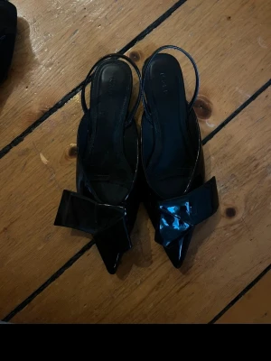 Svarta låga pumps med rosett - Säljer ett par svarta pumps med låg klack och spetsig tå, storlek 39