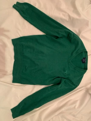 Grön bomullströja från GANT, M - Snygg grön tröja från GANT i storlek M, tillverkad i 100% bomull. Klassisk modell med rund hals och långa ärmar. Diskret GANT-logga broderad på bröstet. Perfekt för dig som gillar stilrena och bekväma plagg.