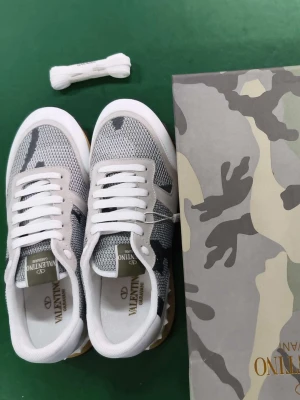 Valentino Rockrunner sneakers camo - Snygga Valentino Rockrunner sneakers med grått och vitt camouflagemönster. Ovandel i mesh och mocka, vita snören och detaljer i vitt skinn. Sulan är beige med svarta partier och har coola nitar bak. Perfekt för dig som gillar streetstyle och exklusiva märken.