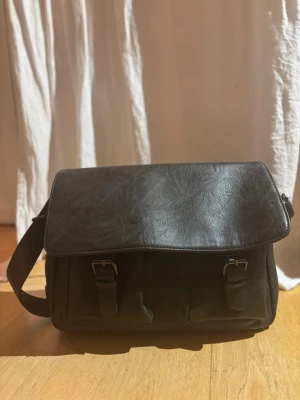 Grå- blå axelväska från Giulia Pieralli - Snygg blå- grå axelväska från Giulia Pieralli i skinnimitation med justerbar axelrem och praktiska fack både fram och bak. Väskan har två spännen framtill och ett rymligt innerfack med dragkedja. Perfekt för dig som vill ha plats för både laptop och småsaker till jobbet eller för skola. 