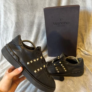 Valentino Garavani Rockstud sneakers - Storlek 40 men passar 41Nypris~6-7000kr Svarta Valentino Garavani Rockstud sneakers i skinn med ikoniska nitar i silver längs sidorna och bak på sulan. Klassisk låg modell med snörning och rund tå. Snygg och edgy design som lyfter vilken outfit som helst. Skorna kommer med originalkartong och extra skosnören. några nitar är borta. undersidan är också lite trasig.