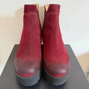 Johnny bulls boots - Snygga vinröda chelsea boots från Johnny Bulls i mocka med kraftig svart platåsula och klack. Skorna har elastiska partier på sidorna för enkel påtagning och en chunky, modern look. Perfekta för dig som vill sticka ut med färg och stil.