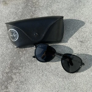 Svarta Ray-Ban Solglasögon  - Snygga svarta Ray-Ban solglasögon i klassisk aviator-modell med svarta glas och tunna bågar. Kommer med original Ray-Ban fodral i svart med diskret mönster. Perfekta för en cool och tidlös look.
