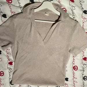 Beige ribbad pikétröja med krage - Snygg beige pikétröja med kort ärm och klassisk krage. Tröjan är ribbad och har en djup v-ringning framtill. Perfekt för en stilren och avslappnad look.