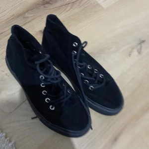 Svarta höga sneakers med snörning - Svarta höga sneakers med klassisk snörning och rund tå. Skorna har en platt sula i gummi och ovandel i tyg. Perfekta för en avslappnad och stilren look. Passar dig som gillar enkel och tidlös stil.