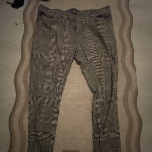 Rutig skinny fit byxa från H&M - Snabb leverans.                                                            Snygga rutig byxa från H&M i skinny fit-modell. Byxorna har grå och svarta toner med klassiskt rutmönster, bälteshällor och fickor både fram och bak. Perfekt för dig som gillar en smalare passform och vill sticka ut med ett stilrent mönster.