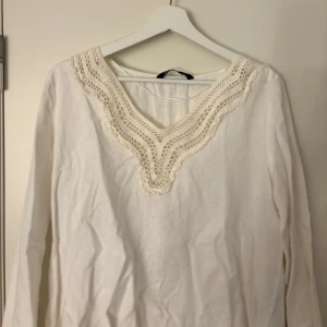 Vit blus med spetsdetaljer - Säljer en vit blus med v-ringning och breda ärmar. Blusen har fina virkade spetsdetaljer runt halsen! Aldrig använd och ganska stor i storleken