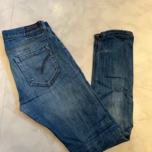 Dondup Jeams - Säljer ett par blå  jeans från Dondup med slitningar och hål på benen för en cool, avslappnad look. Jeansen har klassiska fem fickor, orangea sömmar och är tillverkade i bomullsmix med stretch. Perfekta för dig som gillar en smal passform och streetstil.