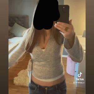 Grå omlottkofta från Gina Tricot XS - Supermysig grå omlottkofta från Gina Tricot i ullblandning. Koftan har långa ärmar, v-ringning och knyt i sidan för en snygg passform. Perfekt till lager-på-lager och ger en chill men ändå stilren vibe.