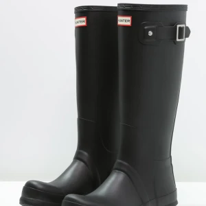 Svarta Hunter stövlar  - Säljer mina hunterstövlar då de tyvärr inte passar. Köpta på NK. Klassiska svarta höga stövlar i gummi med justerbart spänne på sidan. Perfekta för regniga dagar och festivaler. Snygg och tidlös design med Hunter-logga framtill. Nypris 1600