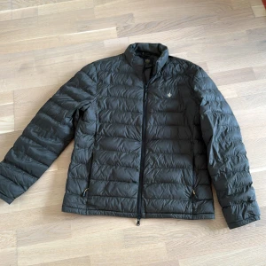 MORRIS JACKA - Säljer en svart dunjacka från Morris med stilren design och diskret logga på bröstet. Jackan har quiltad yta, hög krage och hel dragkedja framtill. Perfekt för kalla dagar och har två fickor med dragkedja. Den är Oanvänd och bevarats i garderob!