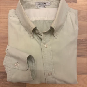 Ljusgrön skjorta från J.Lindeberg - Klassisk ljusgrön skjorta från J.Lindeberg med button down-krage och vita knappar. Tillverkad i mjuk bomull för hög komfort. Långärmad modell som ger en clean och stilren look – perfekt både till vardag och mer dressade tillfällen.  Mått: 	•	Axel till axel: 45 cm 	•	Armhåla till armhåla: 56 cm 	•	Armlängd: 64 cm 	•	Längd: 74 cm