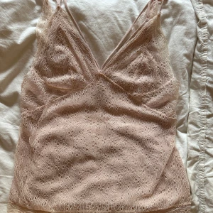 Ljusrosa spetslinne - Säljer ett ljusrosa linne med tunna axelband och v-ringning. Hela toppen är täckt av fin spets med små broderade blommor, vilket ger en romantisk och feminin känsla. Perfekt att styla med jeans eller kjol för en söt look.❤️💞🥰