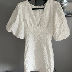 Showpo klänning  - Supersnygg vit kort klänning från Showpo med djup v-ringning och stora puffärmar. Klänningen har en strukturerad yta och markerad midja som ger en riktigt trendig siluett. Perfekt för dig som vill sticka ut och känna dig extra fin. Insydd så den passar snarare än 32 än en 34 men står 34 i! Aldrig använd med prislapp kvar💕